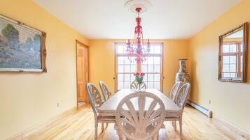 A dining room with a wooden table, chairs, a chandelier, and a vase with flowers.