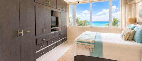 A bedroom with a bed, a ceiling fan, a TV, and a view of the ocean.