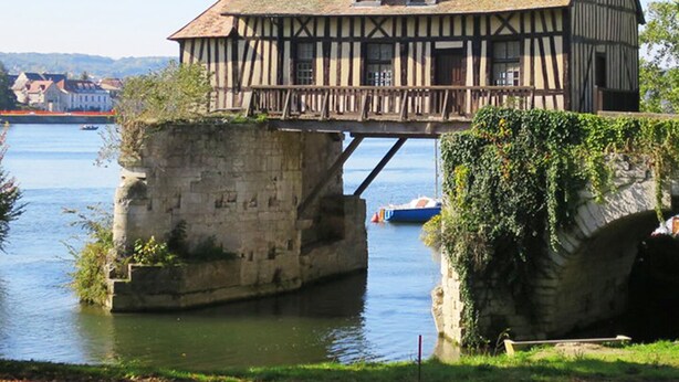 Un edificio histórico con estructura de entramado de madera, base de piedra y un balcón con vistas al río.