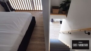Un dormitorio con cama, piso de madera, ventilador y una escalera que lleva a una sala de estar.