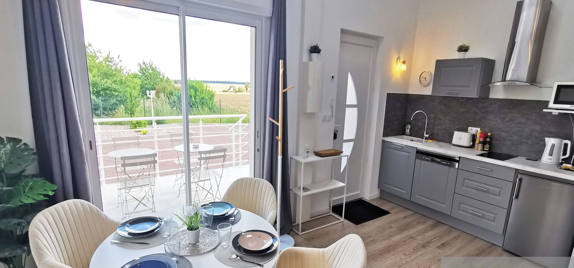 A modern kitchen with grey cabinets, a built-in oven, and a dining area with a round table and chairs.