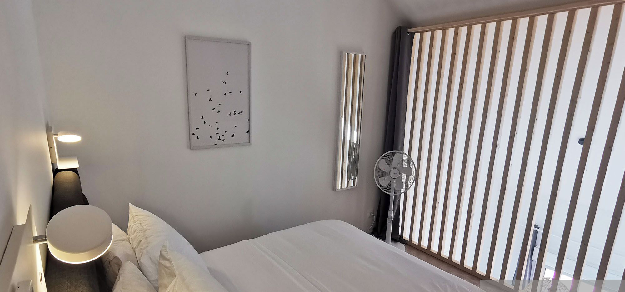 Un dormitorio moderno con cama, mesita de noche, lámpara y ventana con persianas.