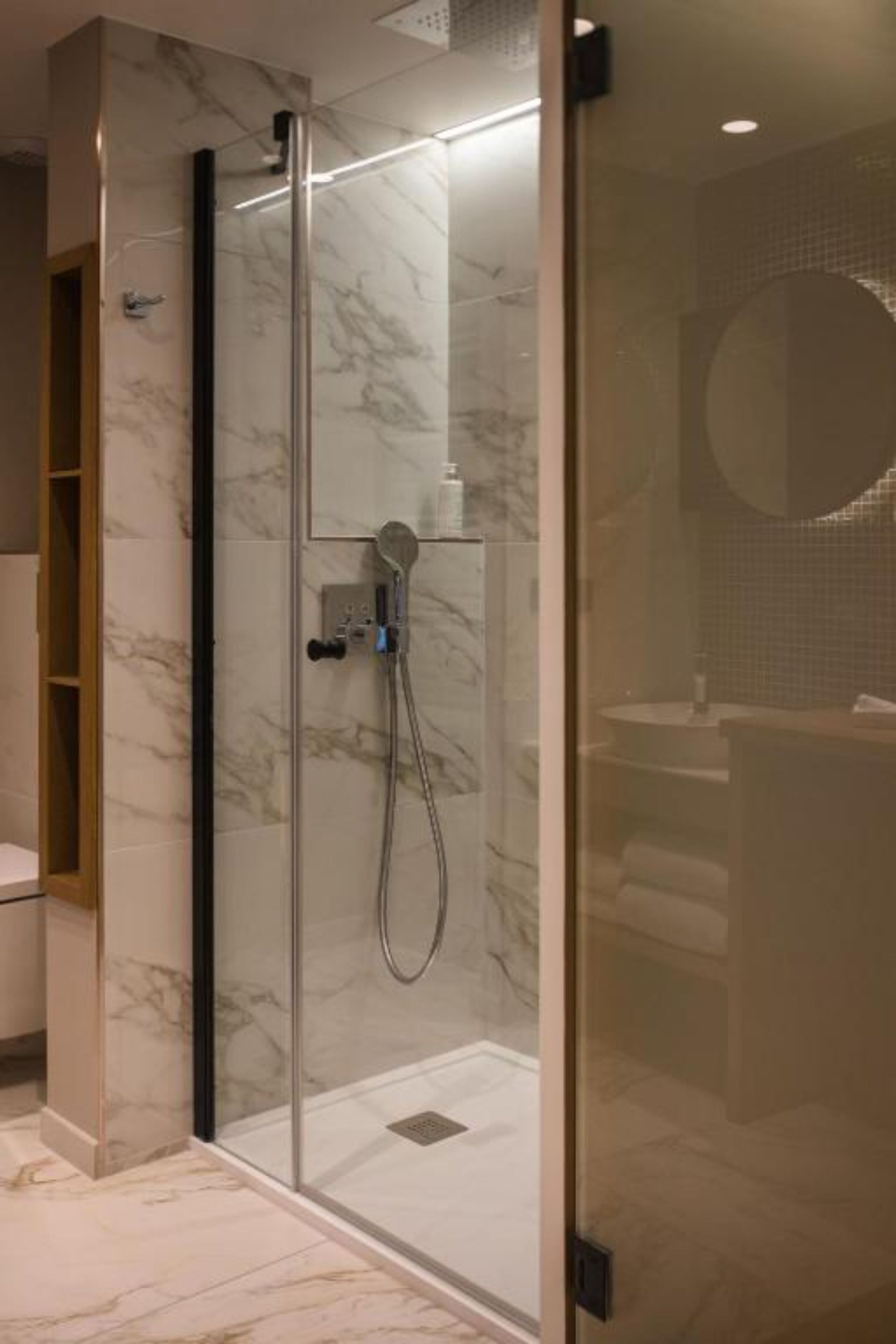 A modern bathroom with a glass-enclosed shower, marble walls, and a round mirror.