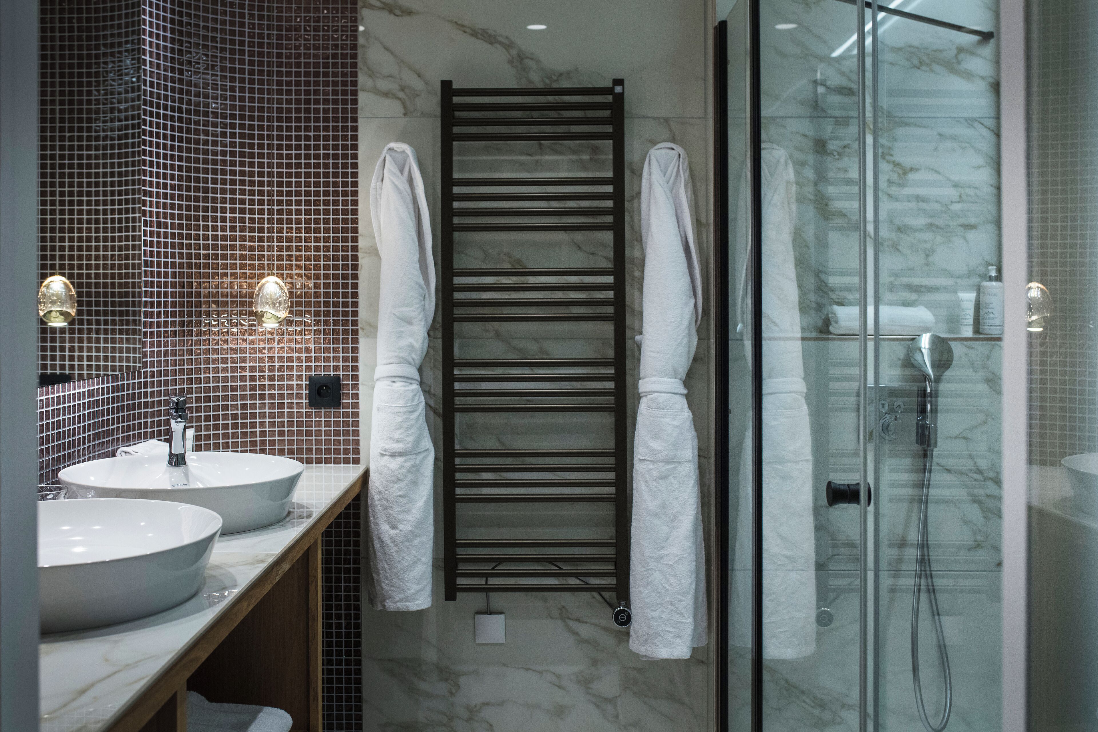 A modern bathroom with two sinks, a towel rack, and a glass shower enclosure.
