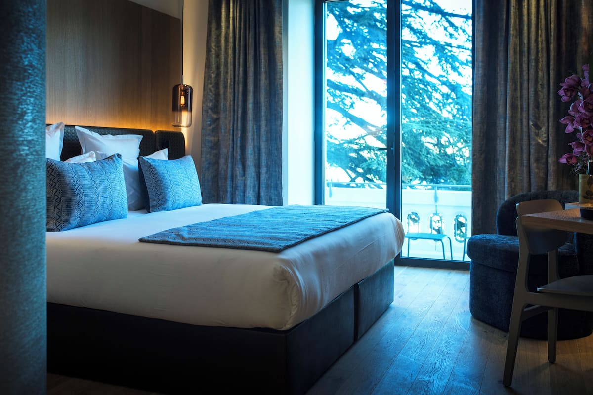 Una habitación de hotel moderna con una cama grande, un rincón de descanso y vistas a árboles por la ventana.