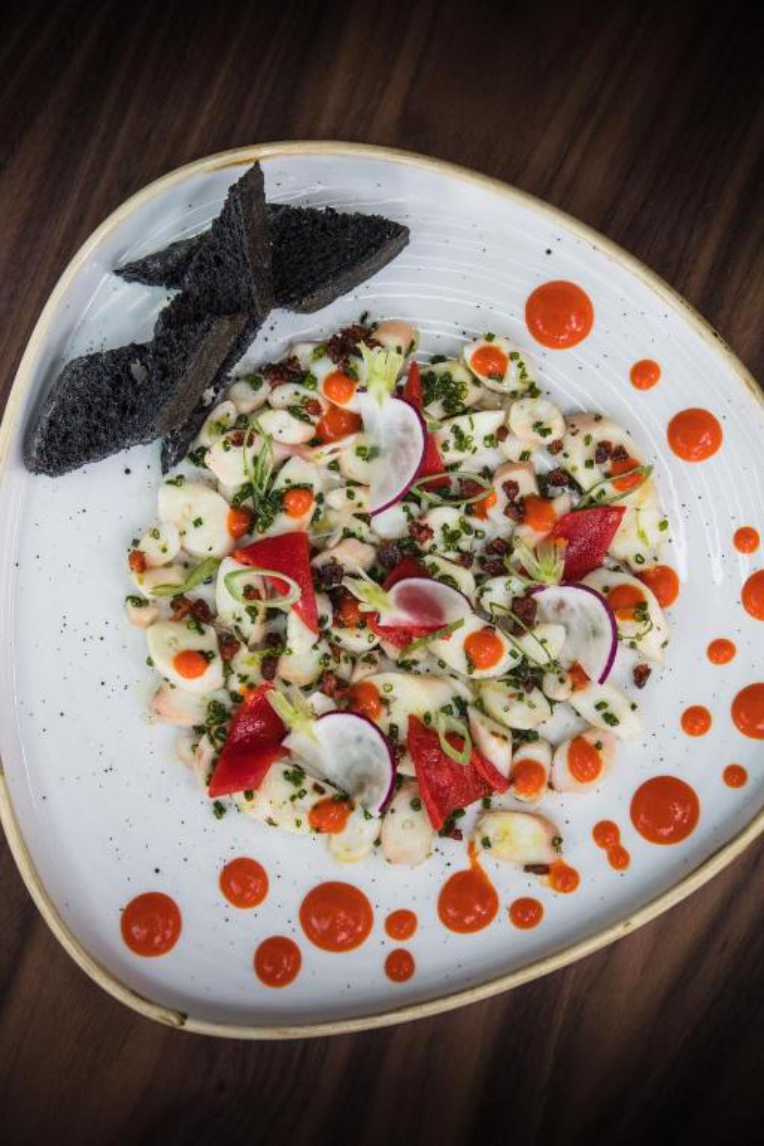 A white plate with a seafood salad, radishes, and a dark garnish on a wooden table.