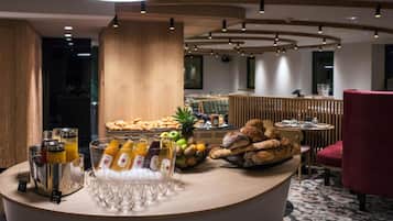 Un buffet de petit-déjeuner proposant une variété d’aliments et de boissons, un comptoir en bois et un espace détente avec une chaise rouge.