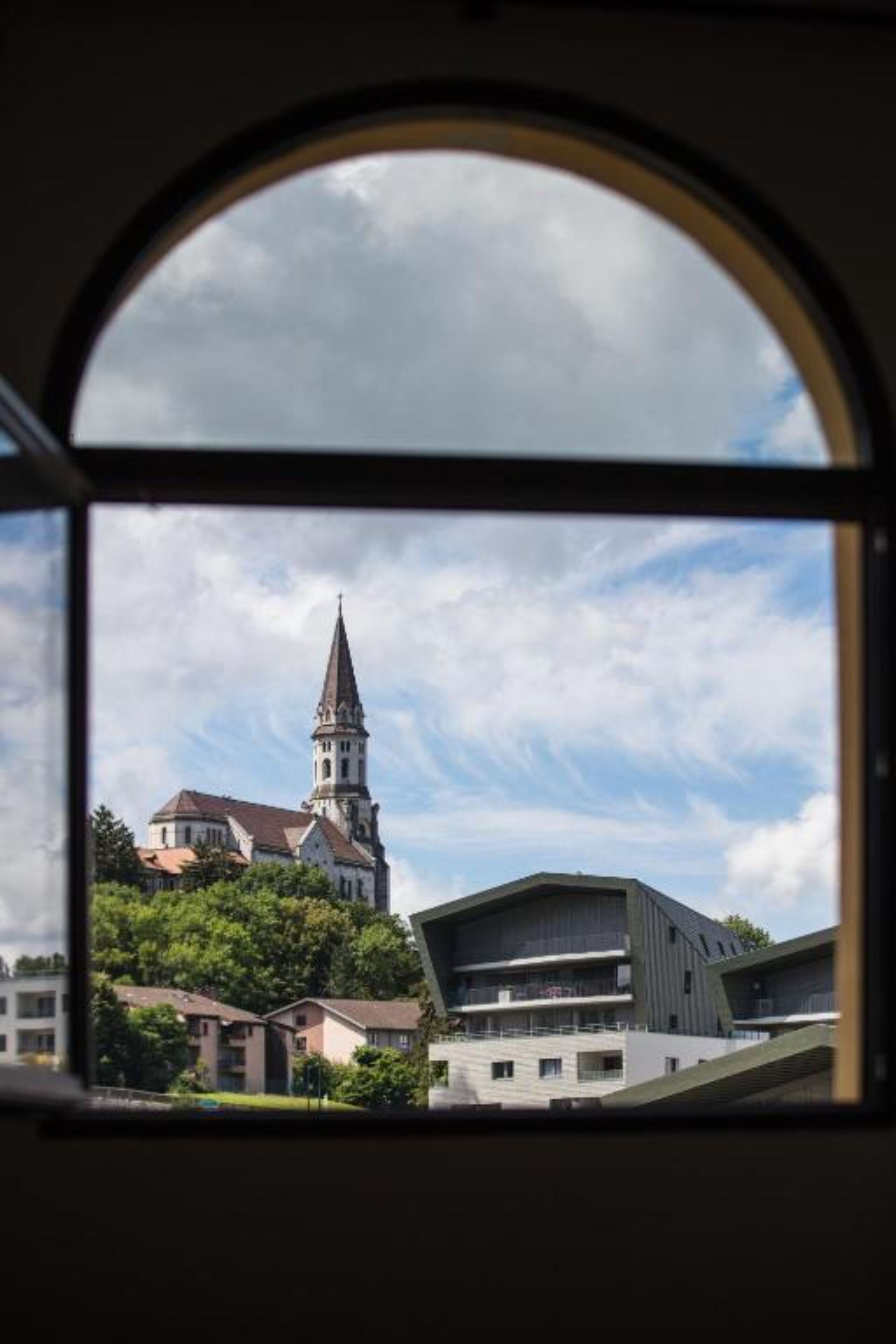 Blick durch ein Fenster auf ein Gebäude mit einem Kirchturm und moderner Architektur.