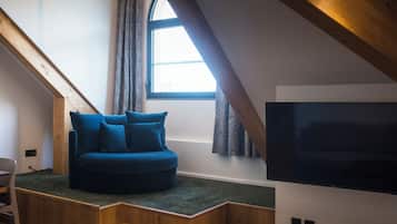 Una habitación acogedora con un sofá azul empotrado, un televisor montado en la pared y una ventana con cortinas.