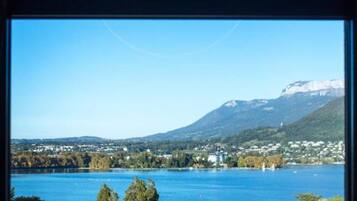 Une vue à travers une fenêtre, avec un ciel bleu dégagé et un lac, des montagnes se dessinant à l’horizon.