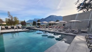 A swimming pool with lounge chairs and umbrellas, surrounded by mountains. - Le Pélican (Annecy)