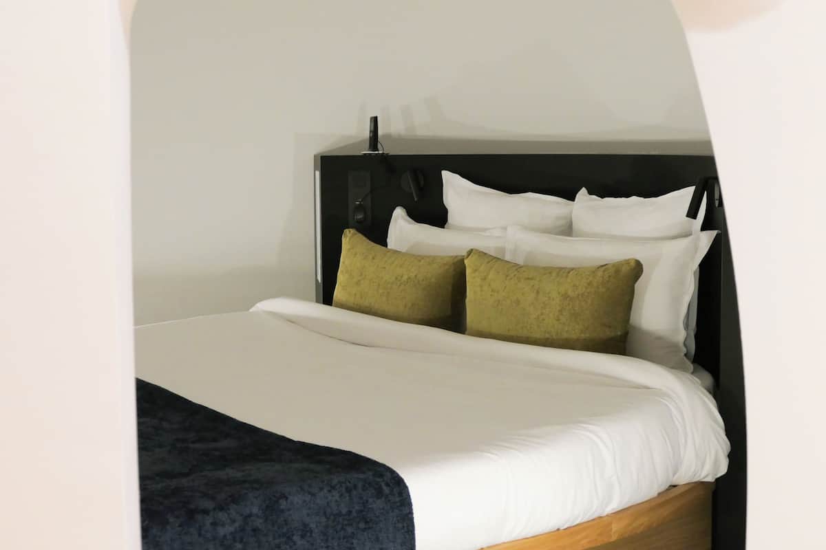 Una cama bien hecha con almohadas blancas y verdes, un cabecero oscuro y un marco de madera.
