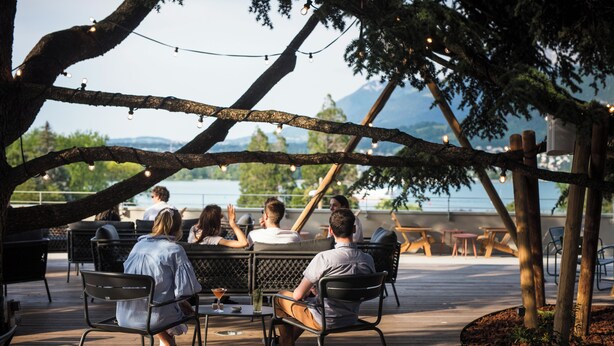 An outdoor seating area with tables and chairs, overlooking a body of water and mountains. - Le Pélican (Annecy)