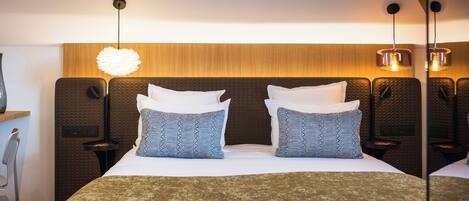Habitación de hotel con una cama grande, dos mesitas de noche, una silla y un cabecero de madera.
