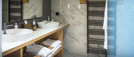 A modern bathroom with two sinks, wooden shelves, and a towel rack.