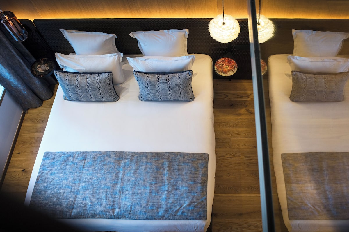 Una cama bien hecha con almohadas blancas y estampadas, una manta azul y un cabecero de madera.