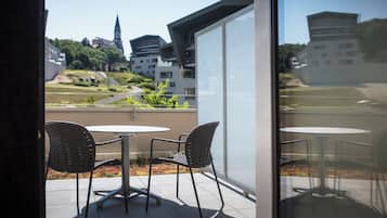 A balcony with two chairs and a table, overlooking a cityscape with buildings and greenery.