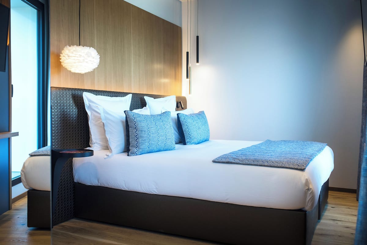 Una habitación de hotel moderna con una cama grande, cabecera de madera y una lámpara de techo con una textura original.