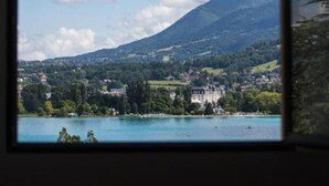 A view through a window of a lake with a mountain in the background and a building on the shore. - Le Pélican (Annecy)