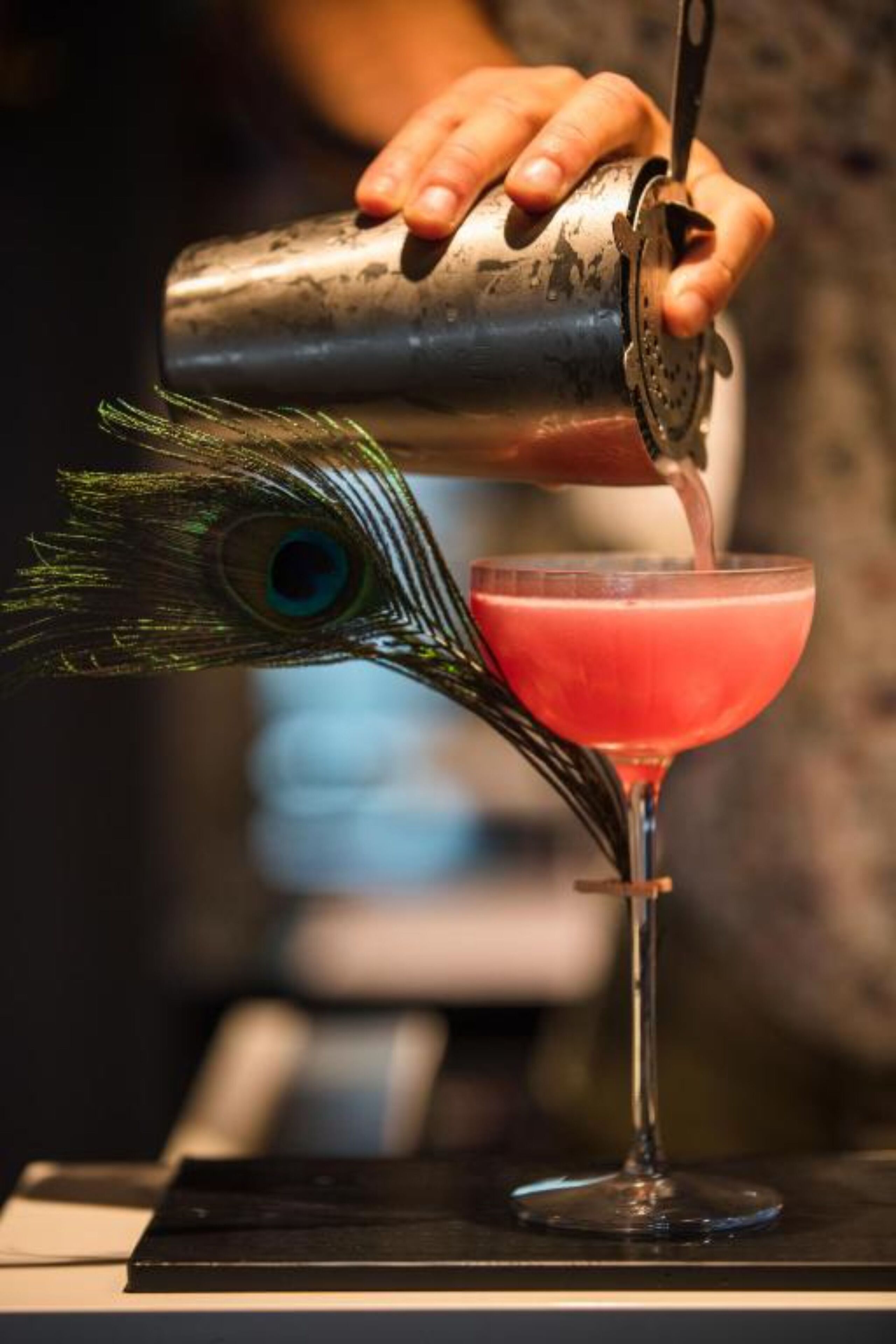 A bartender pouring a drink into a peacock feather-shaped glass.