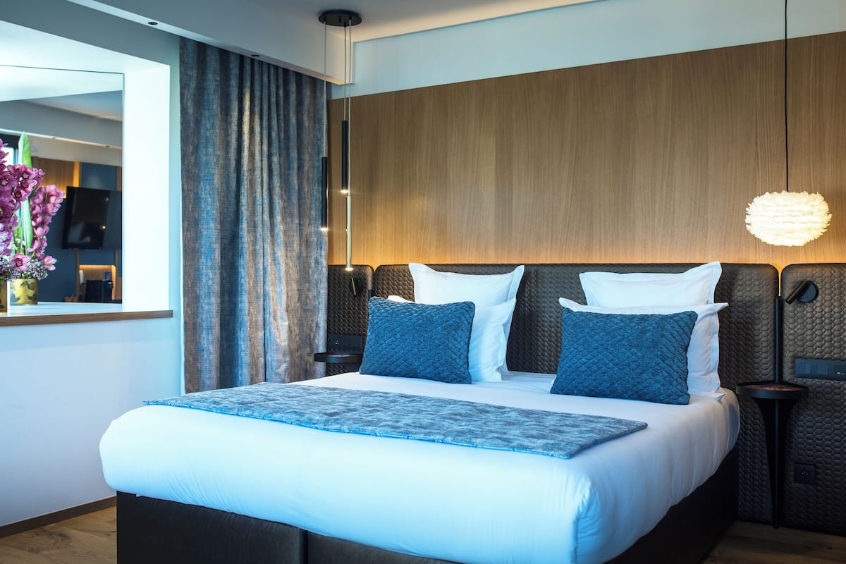 Una habitación de hotel moderna con una cama grande, un cabecero de madera, una mesita de noche y una lámpara colgante.
