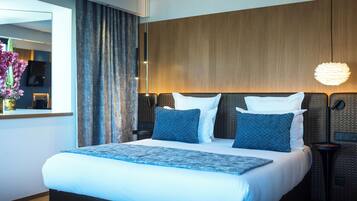 A modern hotel room with a large bed, a wooden headboard, a bedside table, and a hanging light fixture.
