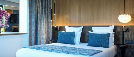 A modern hotel room with a large bed, a wooden headboard, a bedside table, and a hanging light fixture.