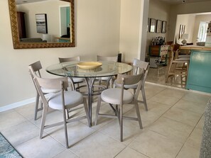 A dining area with a glass table surrounded by six chairs, a large mirror on the wall, and a kitchen in the background.