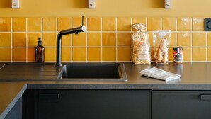 Een keuken met een gele wand, een zwarte spoelbak en een plank met glazen en een karaf.