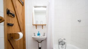 Un bagno con una porta in legno, un lavandino bianco, uno specchio, una doccia e uno sgabello.