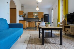 A modern living room with a blue sofa, a wooden coffee table, and a kitchen in the background.