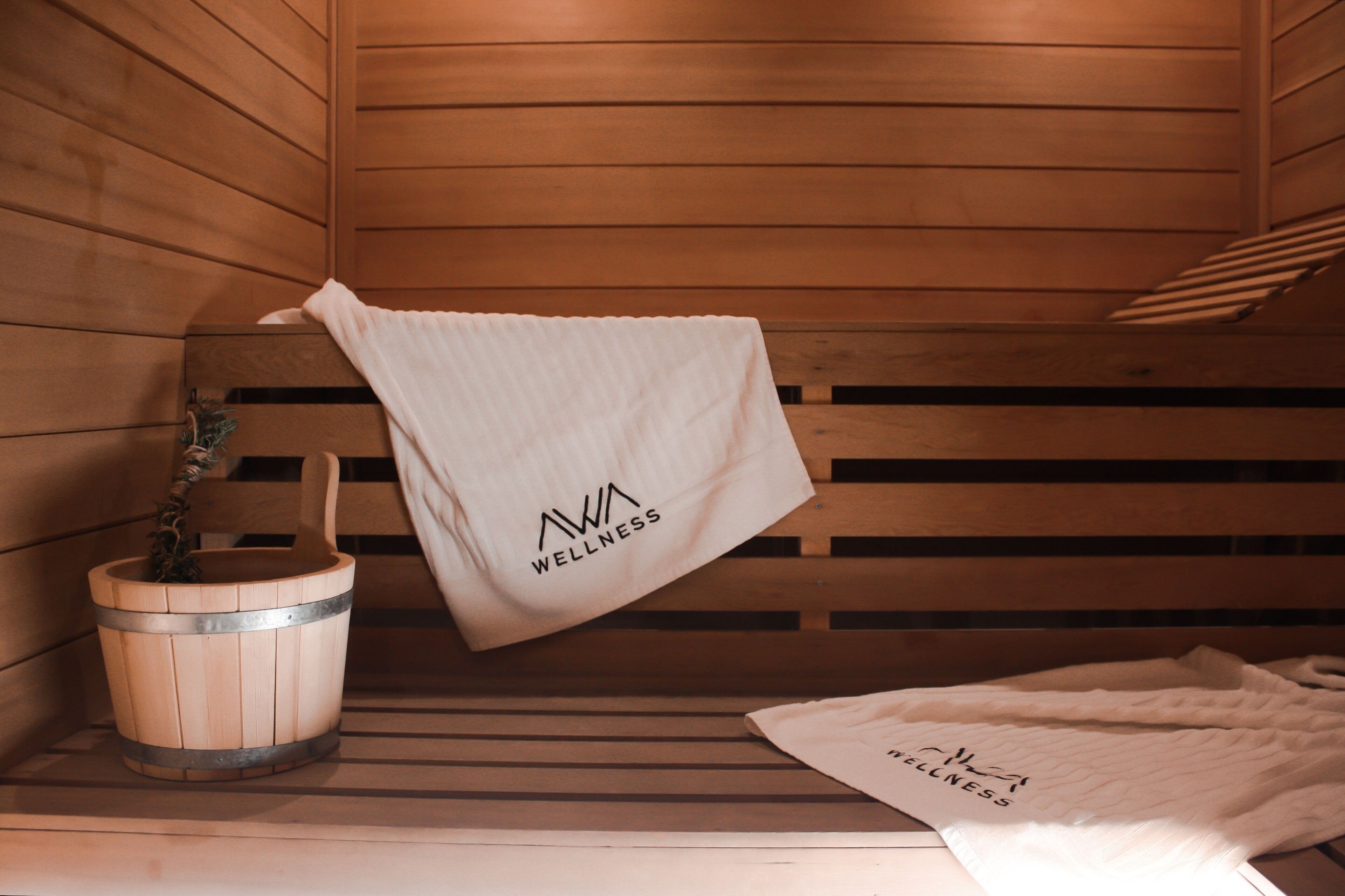 A wooden sauna bench with towels hanging on it and a wooden bucket with a plant.
