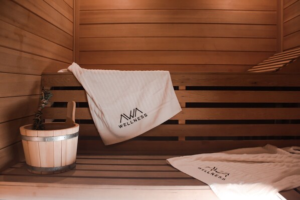A wooden sauna bench with towels hanging on it and a wooden bucket with a plant.