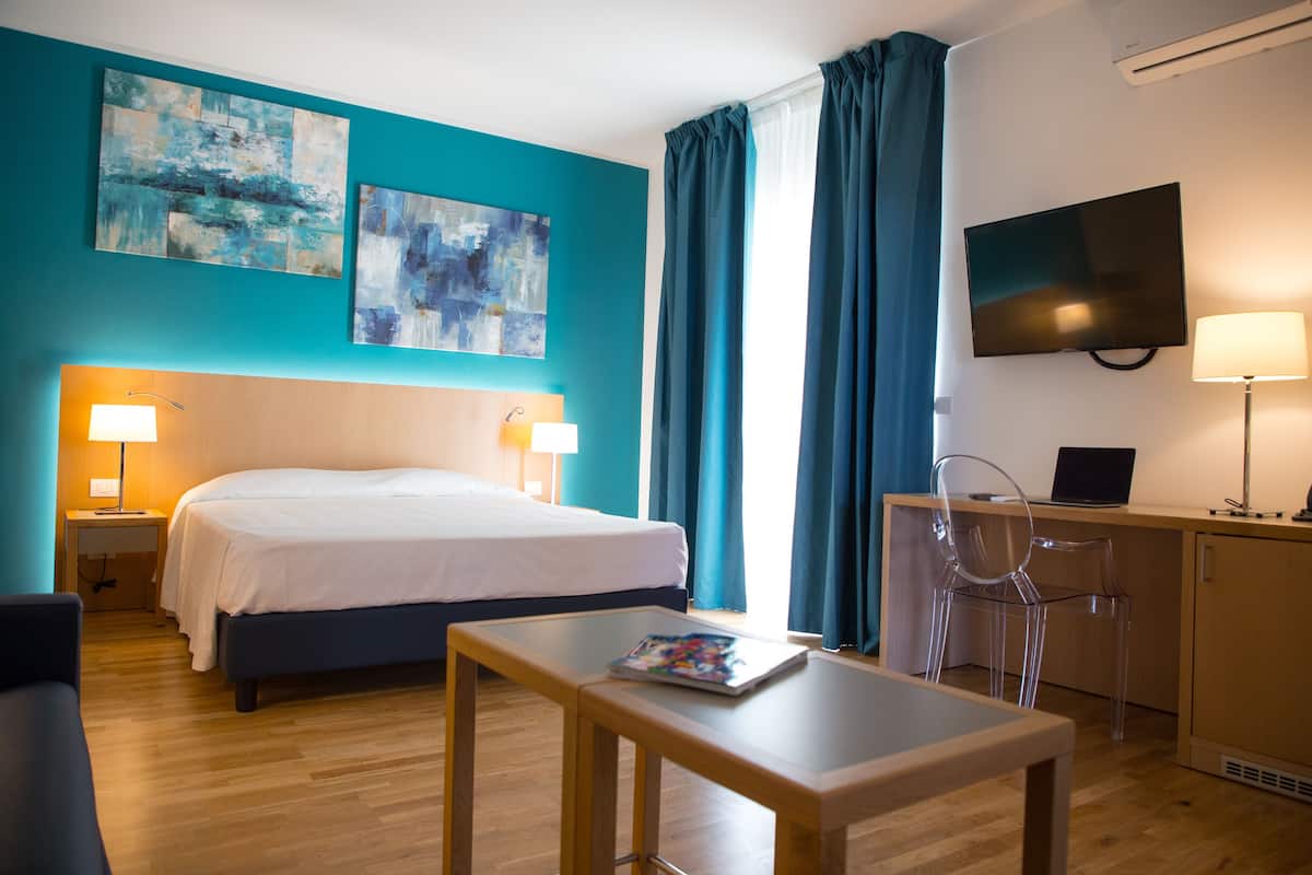 Ein Hotelzimmer mit einem Bett, einem Schreibtisch mit Laptop, einem Fernseher und zwei Bildern an der Wand.