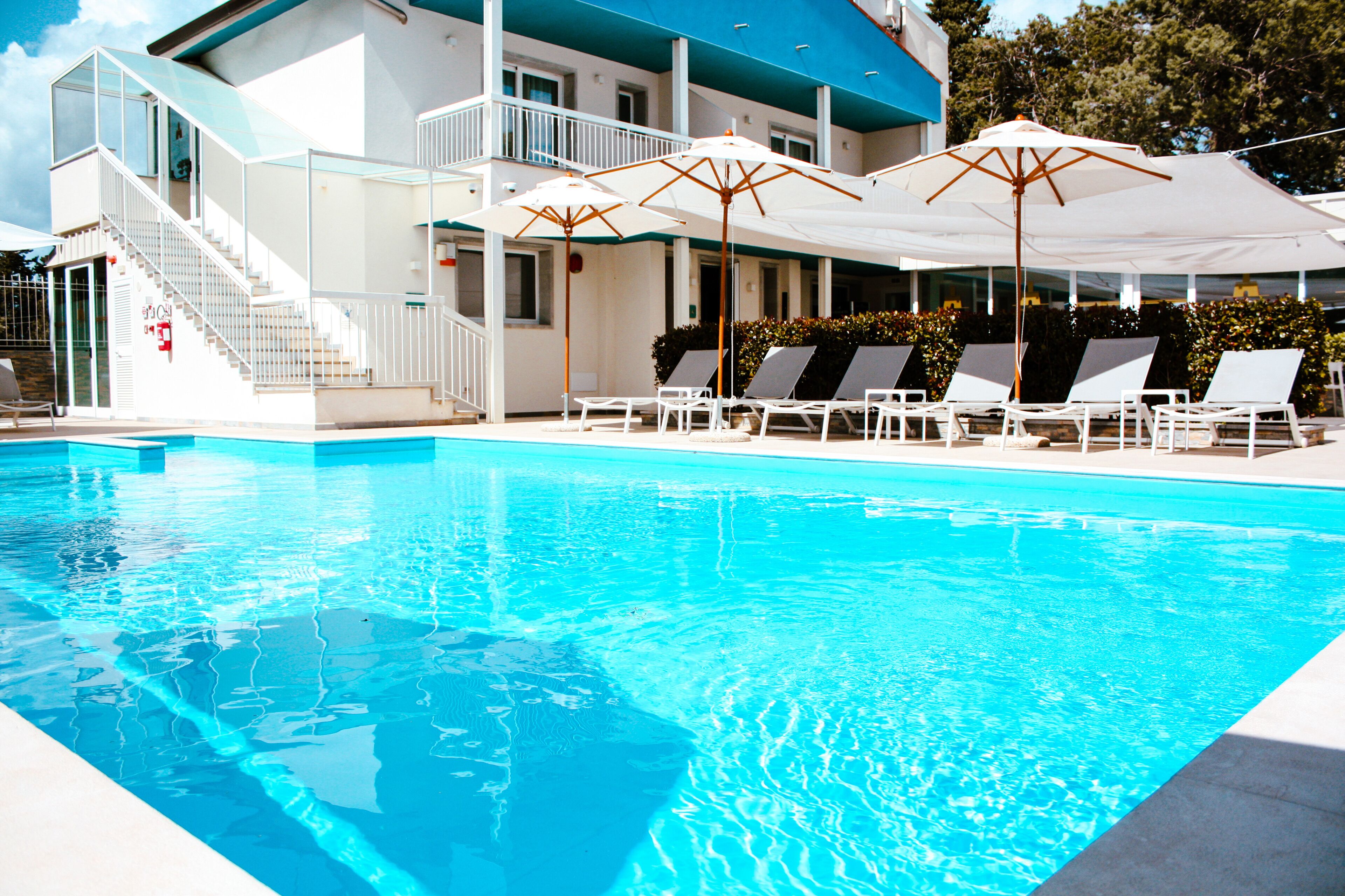 Ein Pool mit weißen Liegestühlen und Sonnenschirmen, eine Treppe und ein Gebäude mit blauem Dach.