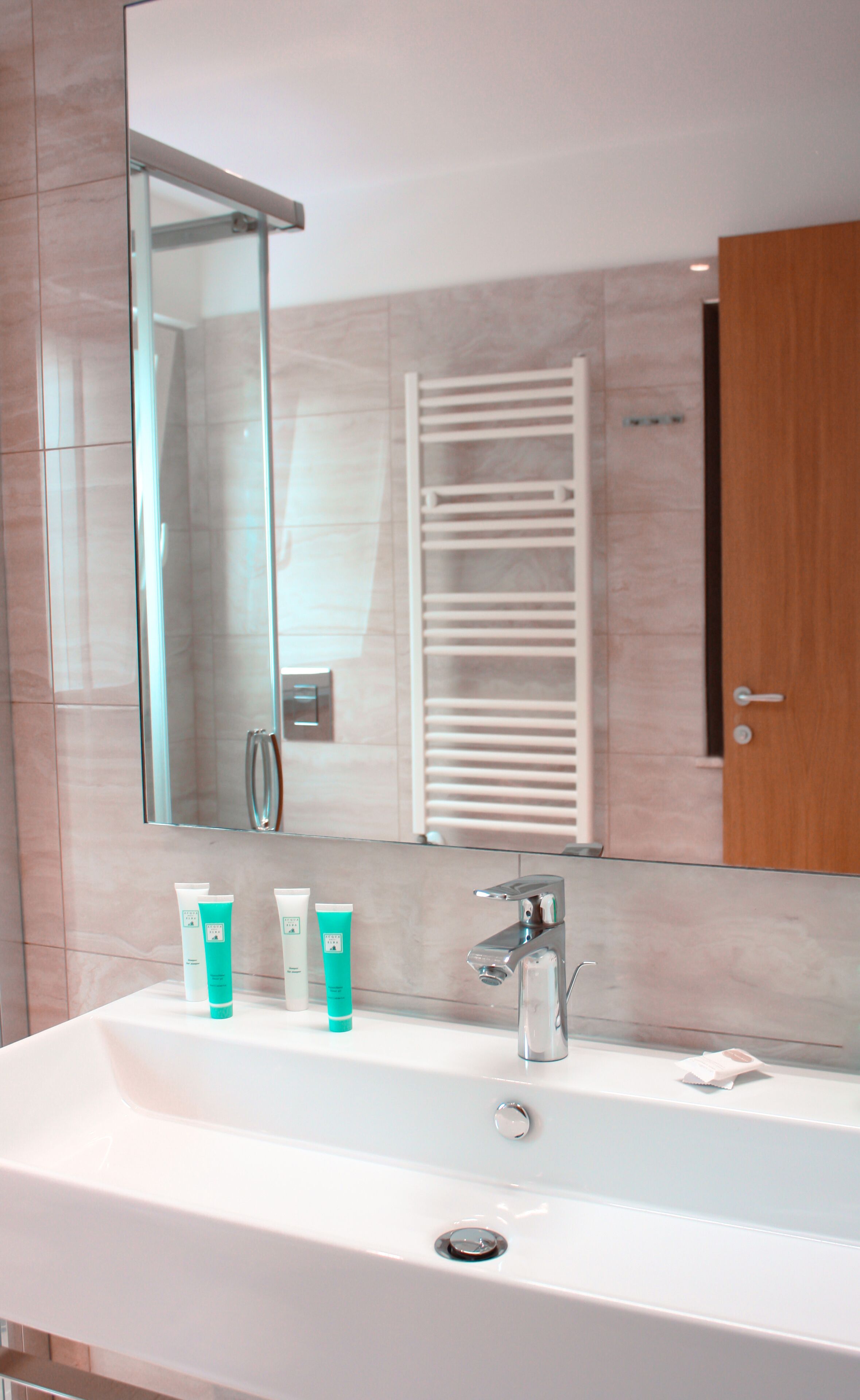 A bathroom with a large mirror, a sink, and toiletries.