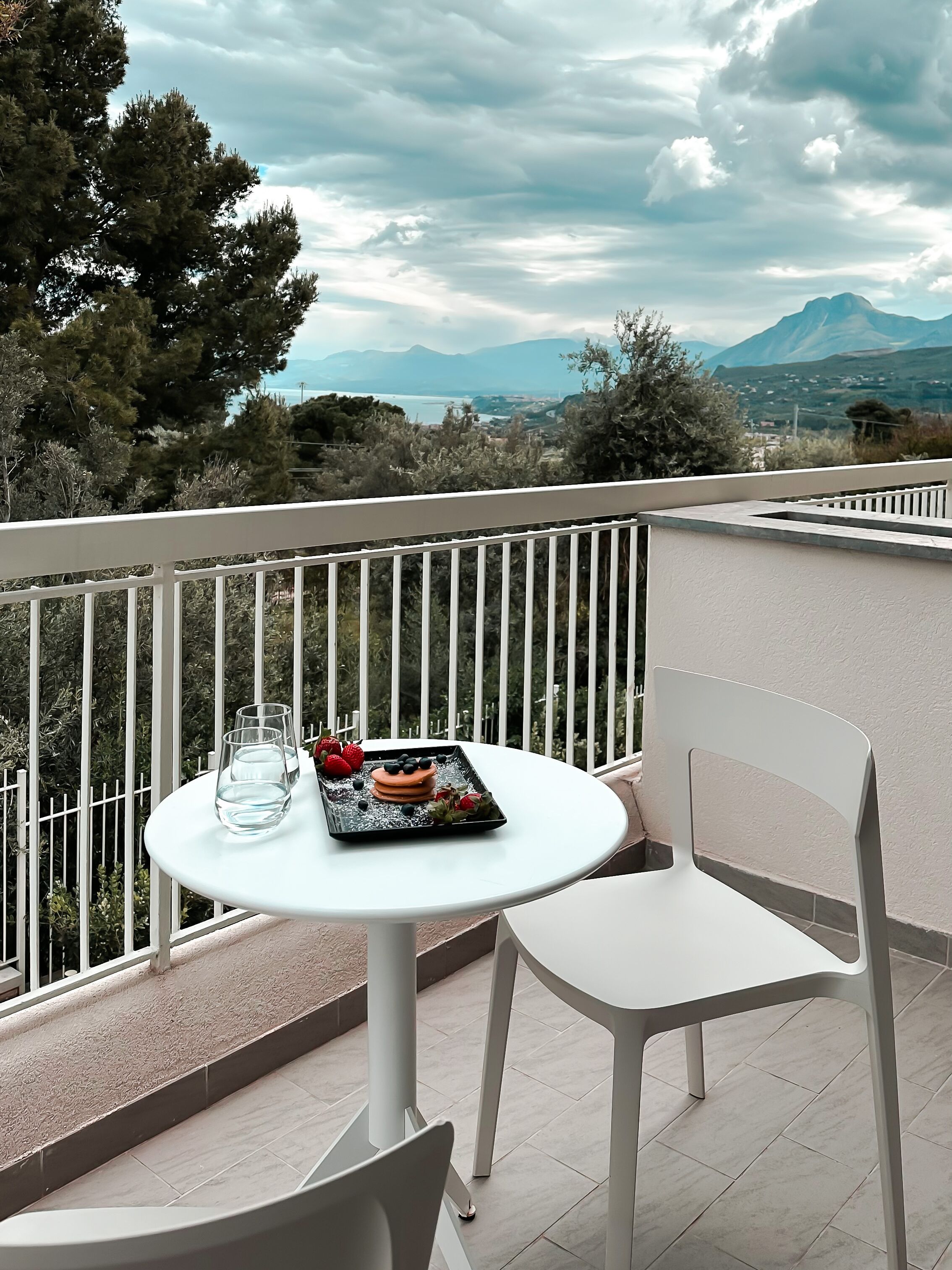A balcony with a round table, a white chair, and a tray with food and drinks.