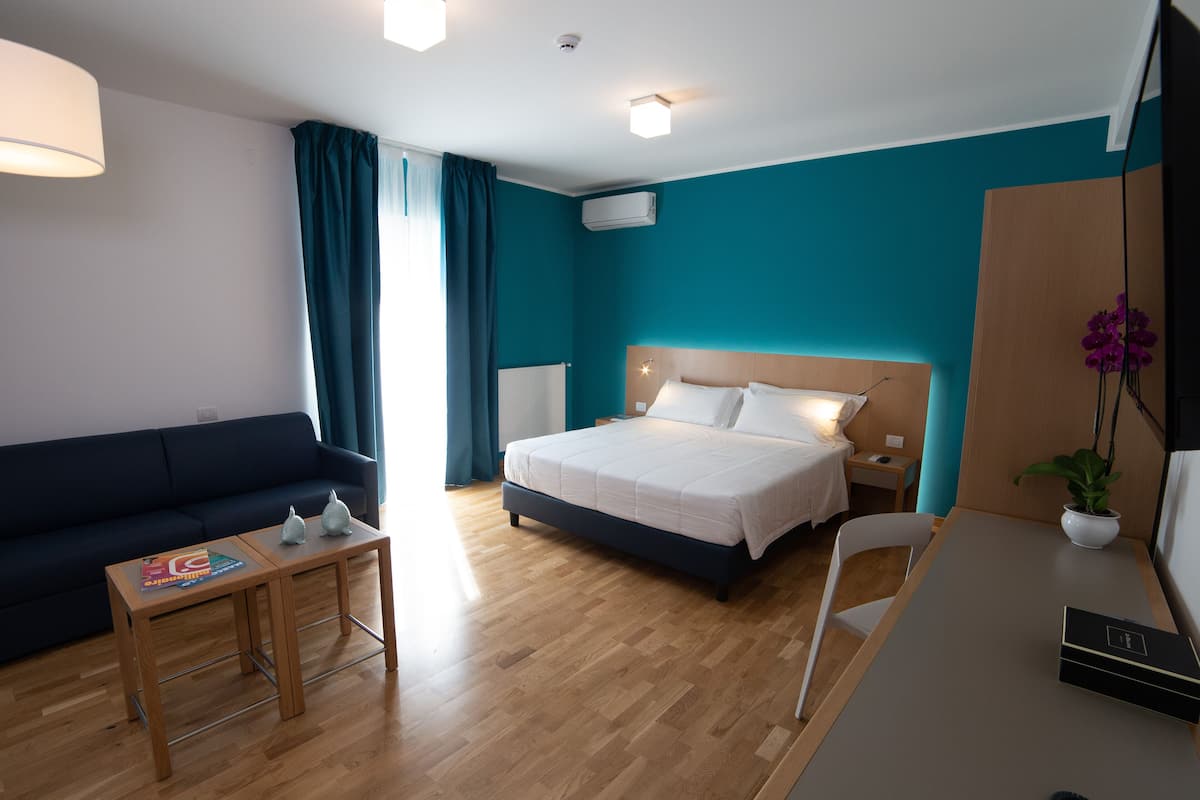 Ein Hotelzimmer mit Bett, Sofa, Schreibtisch und einer Zimmerpflanze.