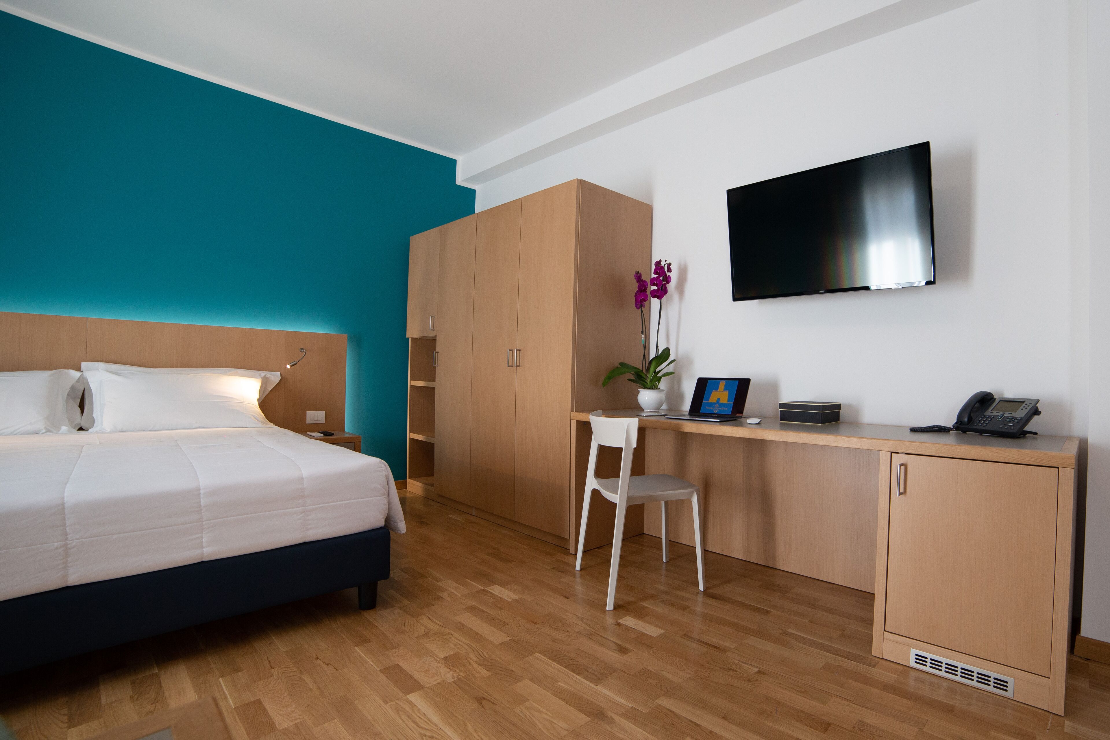A hotel room with a bed, a desk with a chair, a television, and a wardrobe.