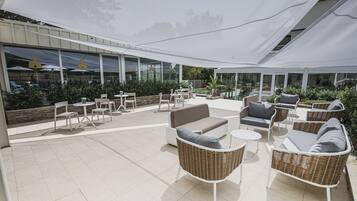 An outdoor patio area with wicker furniture, a white canopy, and a view of a building with large windows.