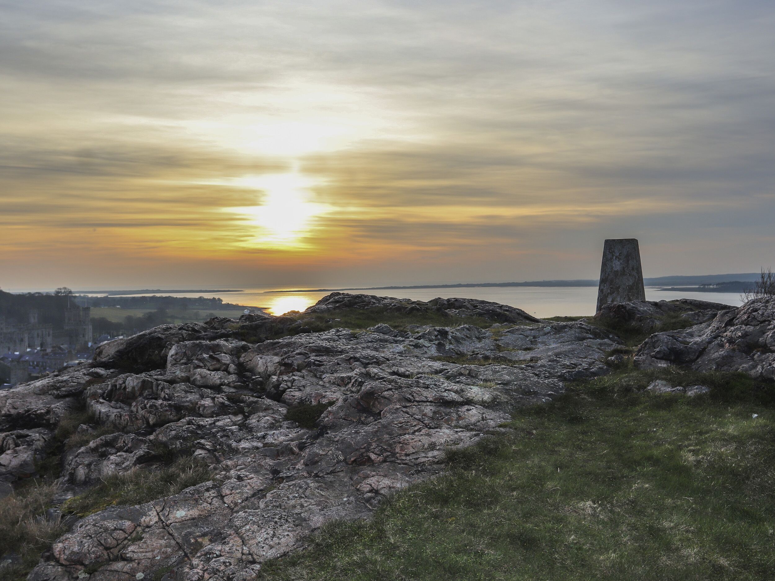 A rocky landscape with a stone monument and a distant view of a city at sunset.