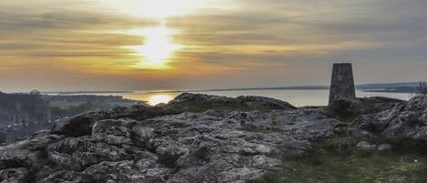 A rocky landscape with a stone monument and a distant view of a city at sunset.