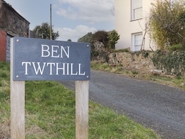 A sign reading "BEN TWTHILL" on a wooden post beside a road.