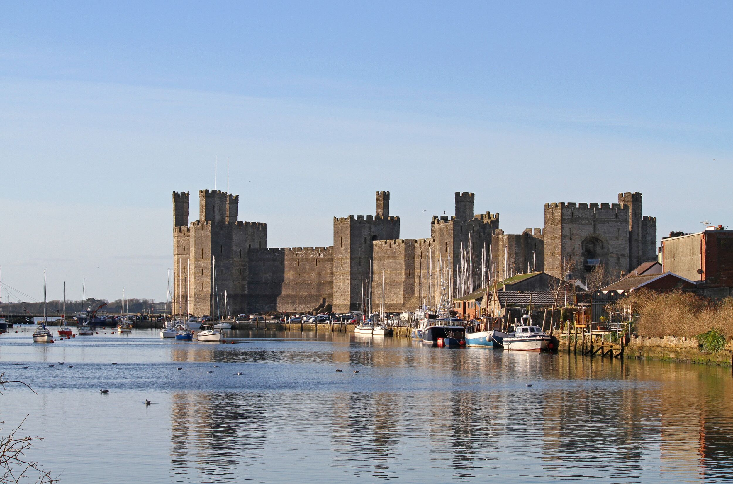 A historic castle with a moat, surrounded by boats and docked vessels.