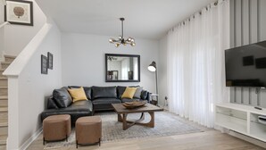 Una sala de estar moderna con un sofá de cuero negro, una mesa de centro de madera y un televisor de pantalla plana sobre un soporte blanco.