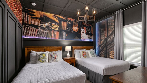 Habitación de hotel con dos camas, una mesita de noche de madera con lámpara, un mural grande en la pared y vista a un puente por la ventana.