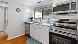 Una cocina moderna con gabinetes blancos, electrodomésticos de acero inoxidable, un microondas integrado y una ventana sobre el fregadero.