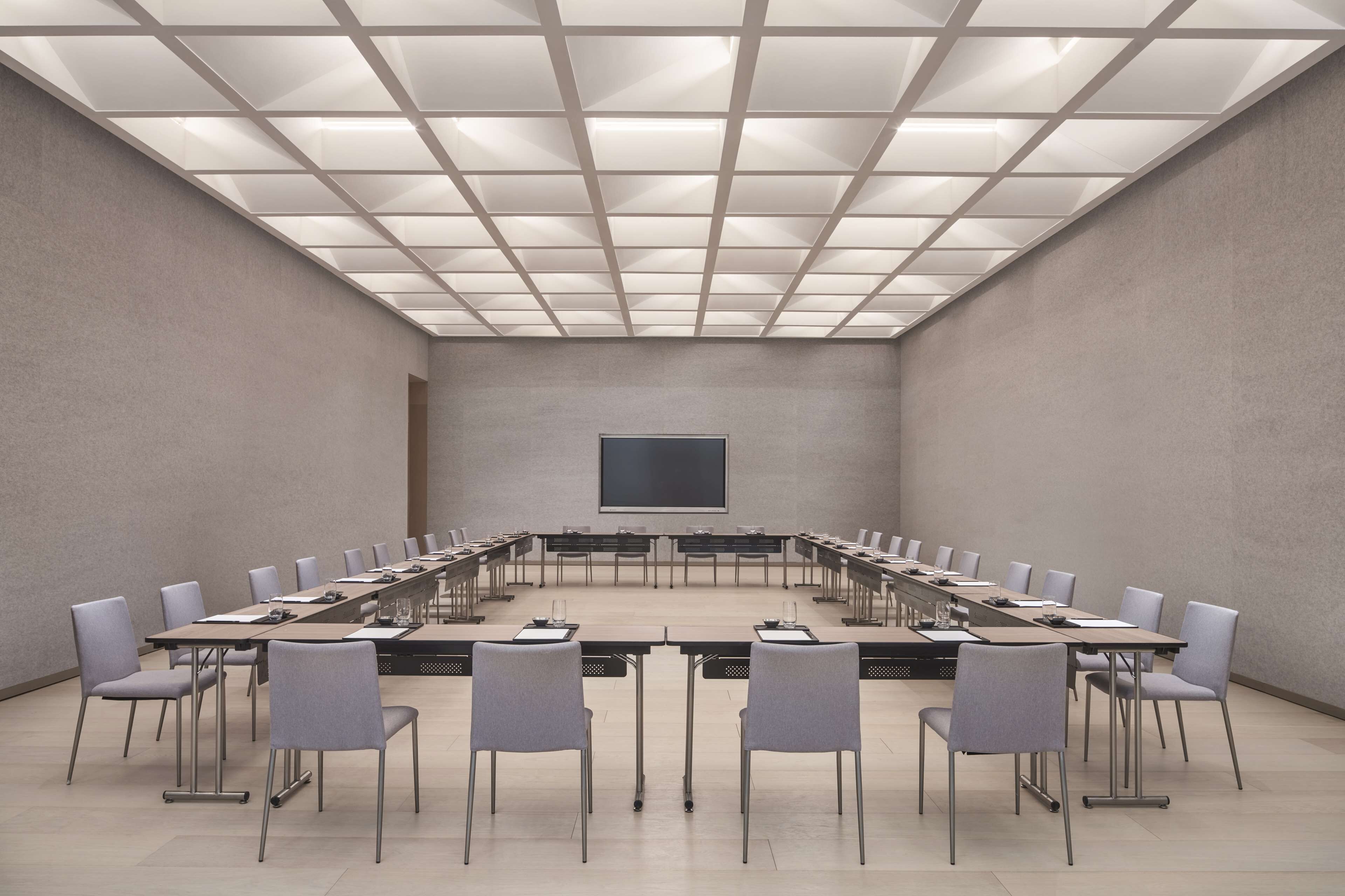 Un salón de conferencias con una larga mesa, sillas, una pantalla de proyector y un techo de baldosas.