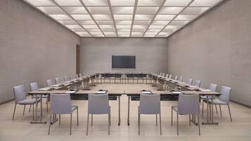 Un salón de conferencias con una larga mesa, sillas, una pantalla de proyector y un techo de baldosas.