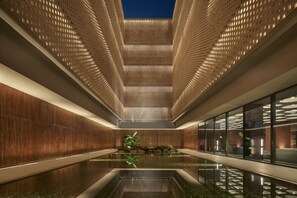 Un interior moderno con una fuente de agua reflectante, paneles de madera y un techo con motivos.